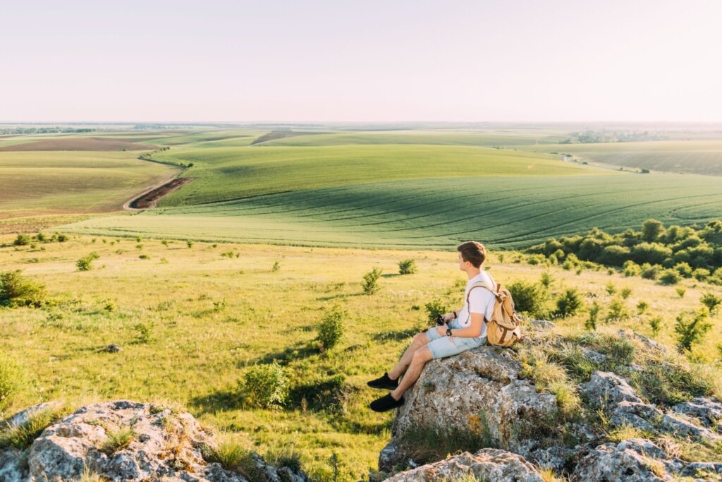 Personne assise au bord d'un rocher à observer la nature au soleil en été